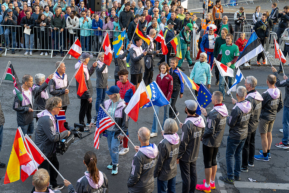 BMW BERLIN-MARATHON 2023: Jubilee-Club delegation at Meet the Legends, marching onto the stage through the flag trellis © SCC Events