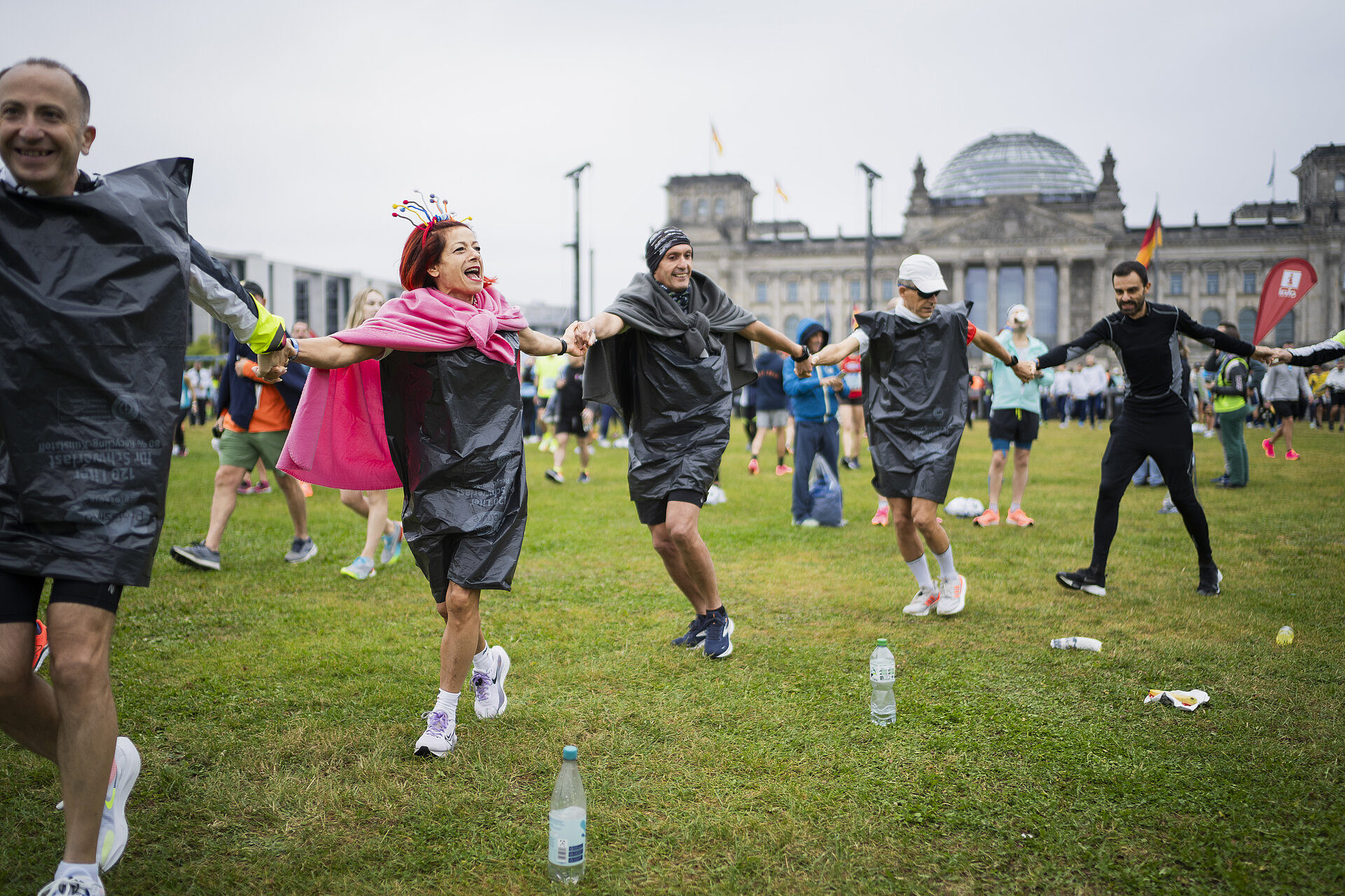 BMW BERLIN-MARATHON 2023: Teilnehmer halten sich an den Händen und laufen beim Aufwärmen im Kreis, im Hintergrund der Reichstag © SCC EVENTS / Sebastian Wells