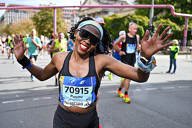 BMW BERLIN-MARATHON 2024: Eine Teilnehmer lächelt voller Freude und winkt in die Kamera © SCC EVENTS / Petko Beier