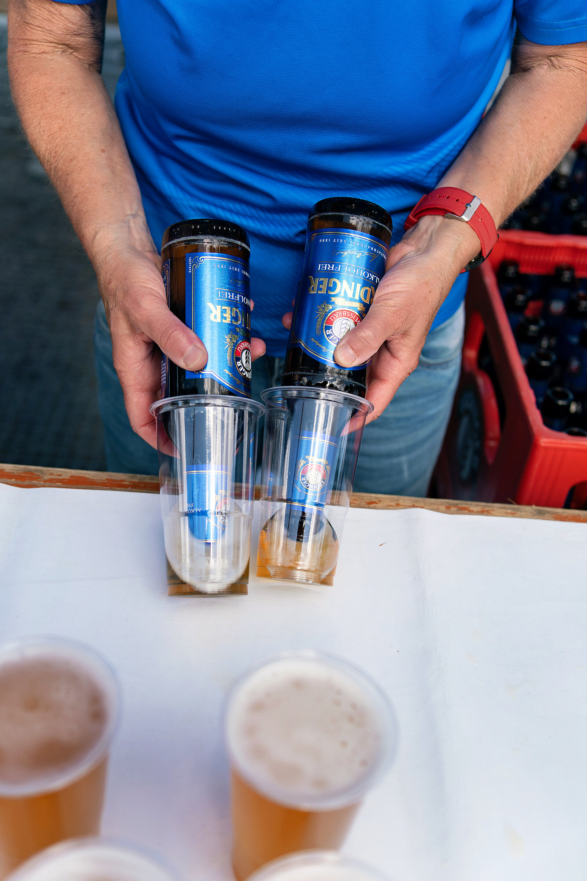 BMW BERLIN-MARATHON course: Male helper pours from 2 bottles of ERDINGER Alkoholfrei into cups © SCC EVENTS / Christian Lietzmann