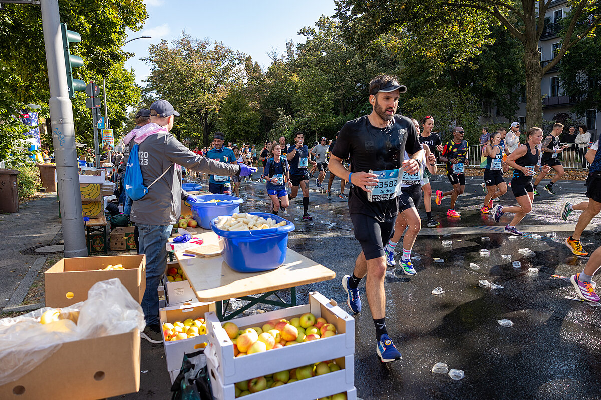  BMW BERLIN-MARATHON 2023: Läufer:innen erhalten an der Verpflegungsstation Obst  © SCC EVENTS / Norbert Wilhelmi