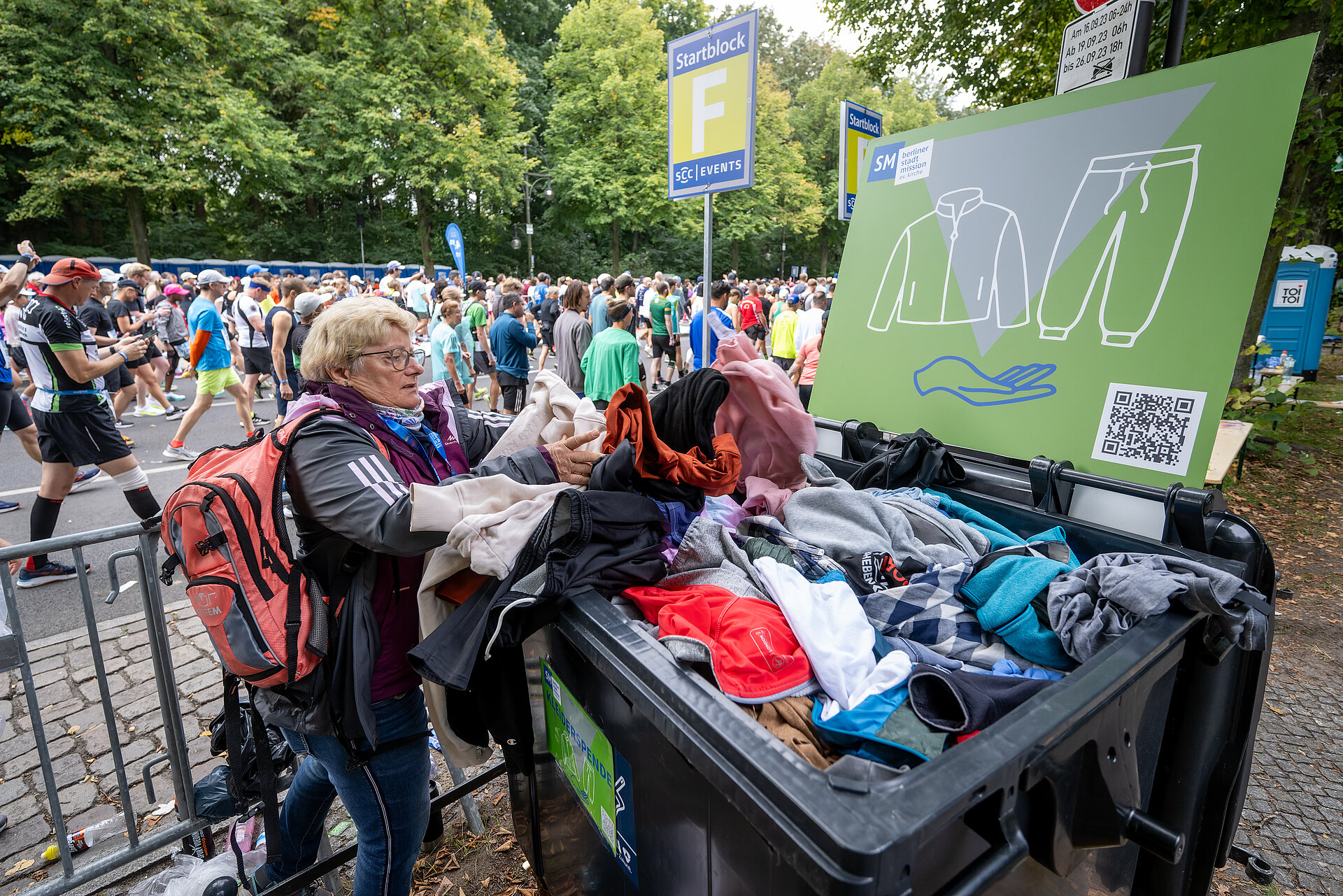 BMW BERLIN-MARATHON Start: Zuschauerin spendet Kleidung und legt diese in eine Tonne © SCC EVENTS